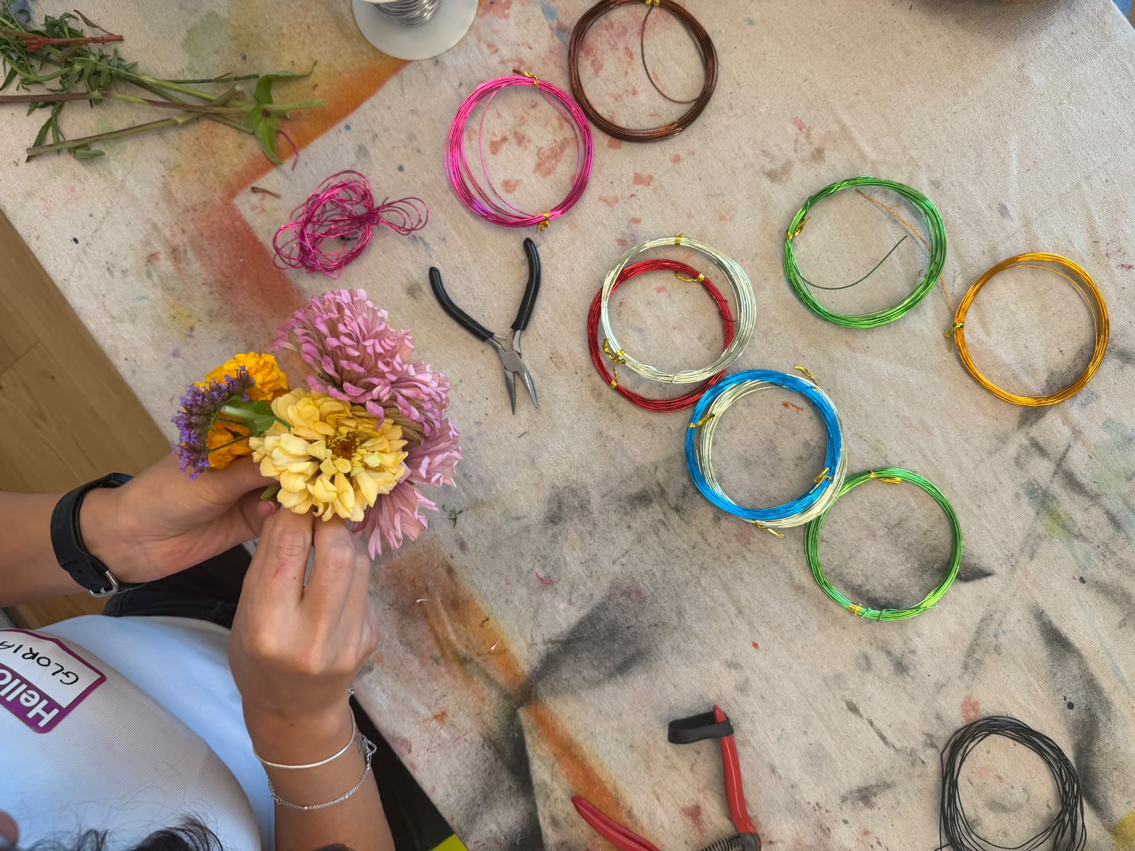 Hands arranging flowers and colored wire on an atelier table